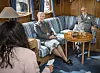 Regentparret sidder i en skibssalon og taler med en journalist ved et rundt bord.