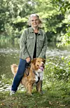 Jannie Rydahl Bjerre står ved en sø med sin hund i grønt parkområde.