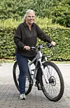 Jannie Rydahl Bjerre står udendørs med en sølvfarvet mountainbike foran en grøn hæk.