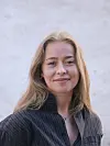 Ung kvinde med langt lyst hår smiler foran en lys væg.