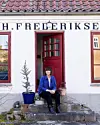 Kvinde sidder på stentrappe foran hvid bygning med rød dør og potteplanter