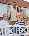 Smilende familie i flere generationer foran hvidt hus med rødt tag