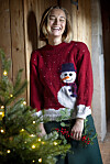 Person i rød julesweater med snemand ved juletræ med lys