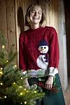 Person i rød julesweater med snemand ved juletræ med lys