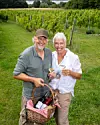 Par med vinglas og fletkurv med vinflasker i en grøn vinmark.