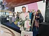 Prisvinder med blomster foran scene med gruppe kvinder og stort pink banner.