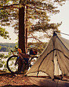 Telt og oppakket cykel i skovkant ved sø på en solrig dag