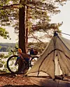 Telt og oppakket cykel i skovkant ved sø på en solrig dag