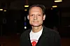 Janus Nielsen står indendørs i mørkt lokale med sort jakke og hvid T-shirt
