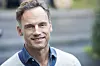 Smilende mand i gråt jakkesætlag og blå skjorte står udendørs