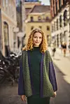 Kvinde i grøn kjole og cardigan går på solrig gade med cykler i baggrunden.