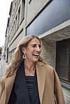 Lis Katz Krefeld i frakke går smilende langs en lys murstensbygning i byen.