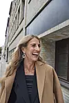 Lis Katz Krefeld i frakke går smilende langs en lys murstensbygning i byen.