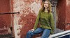 Person i grøn sweater og jeans sidder foran en afskallet rød mur.