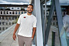Youssef Mohammed står smilende på en tagterrasse ved glasfacade under overskyet himmel.