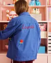 Person i blå jakke med broderet tekst foran pink reol med legetøj og pynt