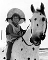 Barn med stråhat sidder på en plettet hest i et sort-hvidt foto