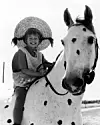 Barn med stråhat sidder på en plettet hest i et sort-hvidt foto