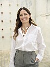 Louise Herping i hvid skjorte står smilende i en lys, rå gårdhave.