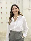 Louise Herping i hvid skjorte står smilende i en lys, rå gårdhave.