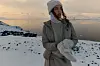 Person i vintertøj står ved snedækket søbred i blødt aftenslys
