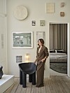 Louise Herping Ellegaard står ved sort stol i lys kunstnerisk stue med vægkunst og kig til soveværelse.