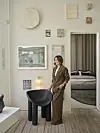 Louise Herping Ellegaard står ved sort stol i lys kunstnerisk stue med vægkunst og kig til soveværelse.
