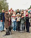 Familie med børn og hund poserer foran boder på et udendørs marked