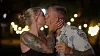 Par med tatoveringer kysser under udendørs lyskæder om aftenen