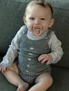 Baby med sut sidder på grøn sofa i strikket sparkedragt
