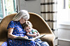 Bedstemor læser bog for barnebarn, der ligger tæt ind til hende i en lys stue
