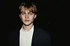 Ung Leonardo DiCaprio i jakke og hvid skjorte foran mørk baggrund, omkring 1993