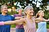 Smilende ældre mennesker laver armstræk i en yogatime i parken.