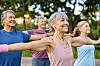 Smilende ældre mennesker laver armstræk i en yogatime i parken.