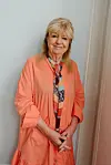 Ulla Terkelsen poserer i koralfarvet kjole ved en lys væg på Kanalhuset