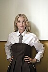 Anne Mette Kirk i skjorte og kjole står med hænderne i siden foran lys væg.