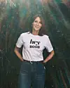 Kvinde i hvid t-shirt med teksten hey BOOB foran grøn bevoksning og solstråler
