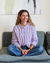 Kvinde i lilla sweater sidder afslappet på grå sofa i lys stue