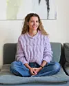 Kvinde i lilla sweater sidder afslappet på grå sofa i lys stue