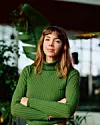 Kvinde i grøn rullekrave står med korslagte arme foran indendørs planter.