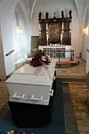 Hvid kiste med blomster foran alter i kirkeinteriør