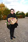 Person med blomsterbuket står på brostensbelagt vej med efterårstræer omkring