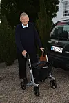 Ældre mand med rollator står ved Fiat-bil foran hvid bygning.