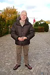 Janus Nielsen står på en brostensbelagt sti med efterårsløv og dansk flag bagved.