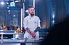 Kok i hvid uniform står ved køkkenbord i et oplyst tv-studie.